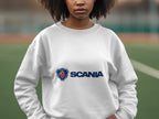 On a sports field, someone wears a unisex white sweatshirt from Garment Graphics featuring a prominent Scania logo, with the blurred background suggesting leisurely outings.