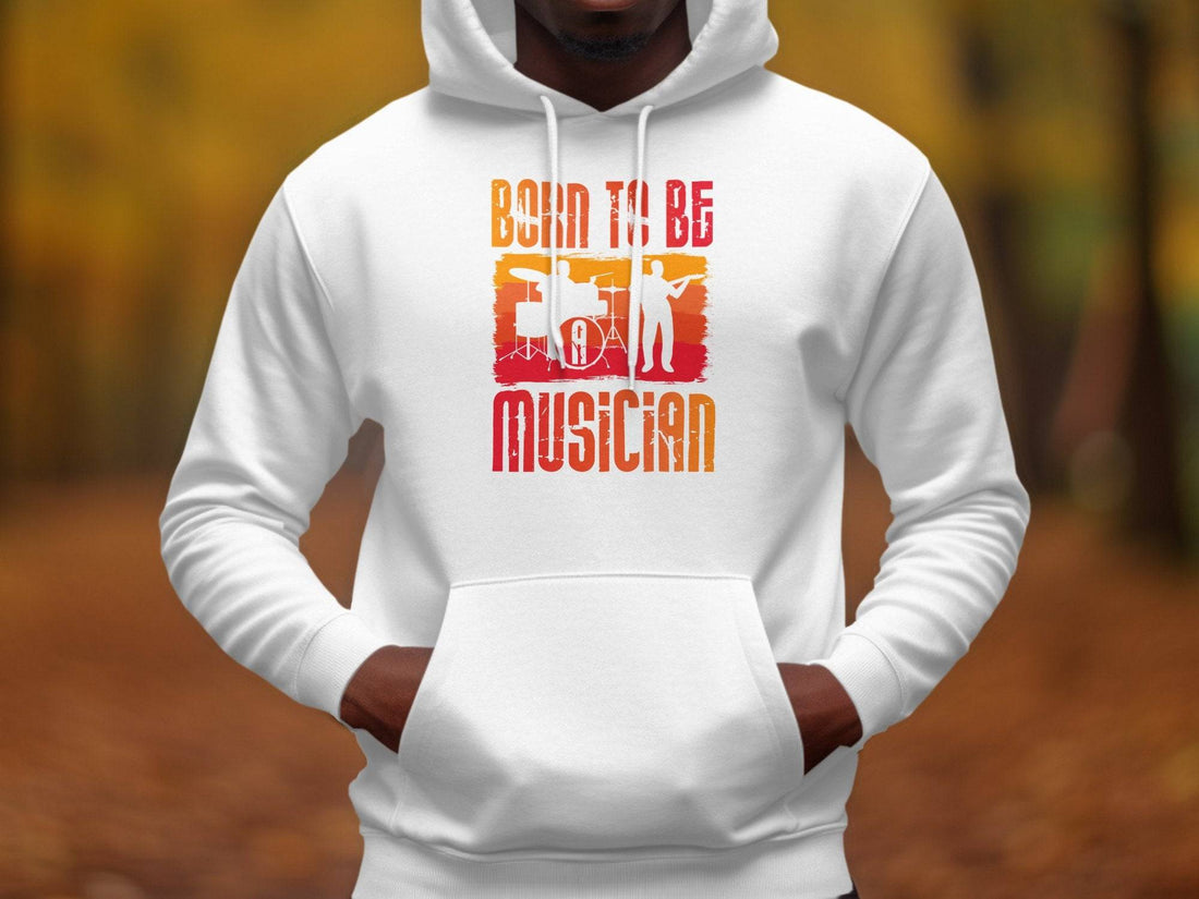 A black Garment Graphics hoodie on a wooden surface, ideal for music lovers, is adorned with an orange and red band member graphic and Born to Be a Musician text. Holiday decorations surround it, while a coffee cup enhances its cozy vibe. Unisex fashion at its best.