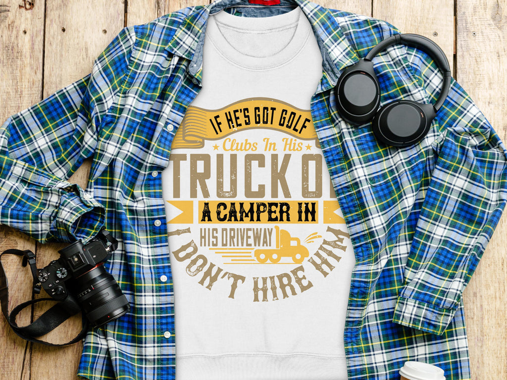 A white Garment Graphics T-shirt with the text If hes got golf clubs in his truck or a camper in his driveway, dont hire him is displayed on a wooden surface. Ideal for outdoor enthusiasts, it’s accompanied by a blue checkered shirt, headphones, and a camera.
