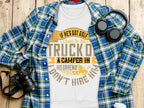 A white Garment Graphics T-shirt with the text If hes got golf clubs in his truck or a camper in his driveway, dont hire him is displayed on a wooden surface. Ideal for outdoor enthusiasts, it’s accompanied by a blue checkered shirt, headphones, and a camera.