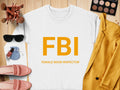 A white Garment Graphics sweatshirt features a bold orange FBI with FEMALE BOOB INSPECTOR below in unisex sizing, styled with a yellow blazer, makeup brushes, eyeshadow palette, sunglasses, nail polish, blue pouch, and pink slip-on shoes on a wooden surface.