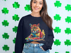 A woman in a Garment Graphics navy sweatshirt with a vibrant big cat design sits against green shamrock decorations. She has long brown hair and wears denim shorts, highlighting her unique style.