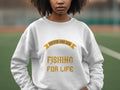 A person wears a white Garment Graphics sweatshirt featuring the phrase Father and Son Fishing for Life in bright yellow, set against a backdrop of blurred greenery and the edge of a sports field.