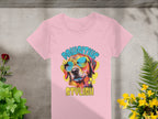 A pink Womens T-Shirt from Garment Graphics features a vibrant dog with sunglasses. PAWSITIVE is printed above and STYLISH below. Its photographed on concrete with small plants and flowers.
