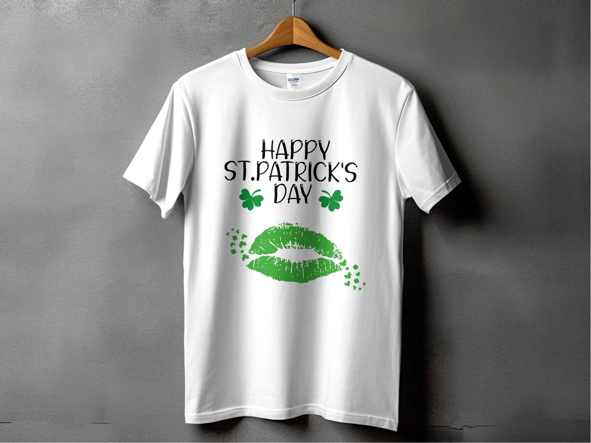 The Garment Graphics T-shirt showcases a festive Happy St. Patricks Day message with green lips and clovers. Hanging against a plain gray wall, it perfectly blends style and celebration.