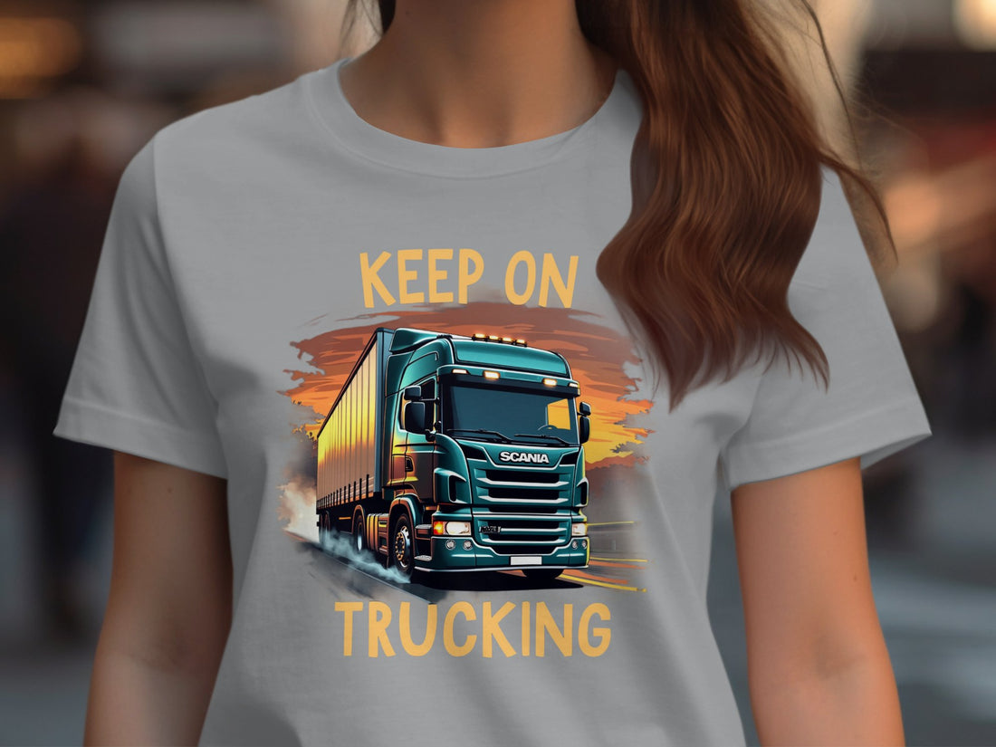 Garment Graphics white t-shirt features a truck design with Keep On Trucking. Its styled amid gifts, pinecones, a candy cane, sweater, and festive decor on wood. Perfect for trucking enthusiasts who enjoy Keep on Trucking T-Shirts during the holidays.