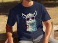 A person relaxes on a bench in a navy blue Llama T-shirt by Garment Graphics, showcasing a llama in sunglasses with No Prob-Llama printed below. The grassy, sandy background is ideal for family outings, with various sizing options available.