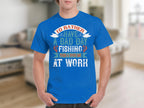 A person in a Garment Graphics blue fishing t-shirt with Id rather have a bad day fishing than a good day at work stands out against the blurred indoor setting, making it a clever gift idea for anglers.