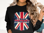 A person with long, wavy hair sports a black Garment Graphics sweatshirt displaying a faded Union Jack and the slogan Dont Blame Me, I Didnt Vote For Him. Unisex sizing offers comfort for everyone.
