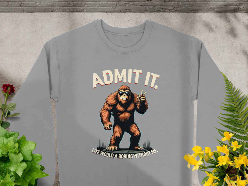This Garment Graphics gray unisex sweatshirt showcases a cartoon Bigfoot making a peace sign, with ADMIT IT above and Life Would Be Boring Without Me below, surrounded by potted plants like ferns and flowering blooms for perfect comfort and style.