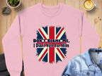 Styled on a wooden surface with a denim jacket, cappuccino, and small plant, Garment Graphics pink sweatshirt showcases a bold, distressed Union Jack design with the text Dont Blame Me, I Didnt Vote For Him.