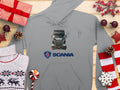 Discover the ultimate Garment Graphics gray hoodie, ideal for truck lovers. Featuring a Scania truck graphic and logo, this design is enhanced with festive decorations such as gift boxes, ornaments, pine cones, candy, and a reindeer-patterned sweater on a wooden backdrop.