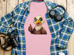 The Garment Graphics Eagle T-shirt, ideal for a casual look, has a cartoon eagle giving a thumbs up on pink fabric. Its styled amidst essentials like a blue and green plaid shirt, headphones, a camera, and a takeaway coffee cup for that classic fit vibe on wood.
