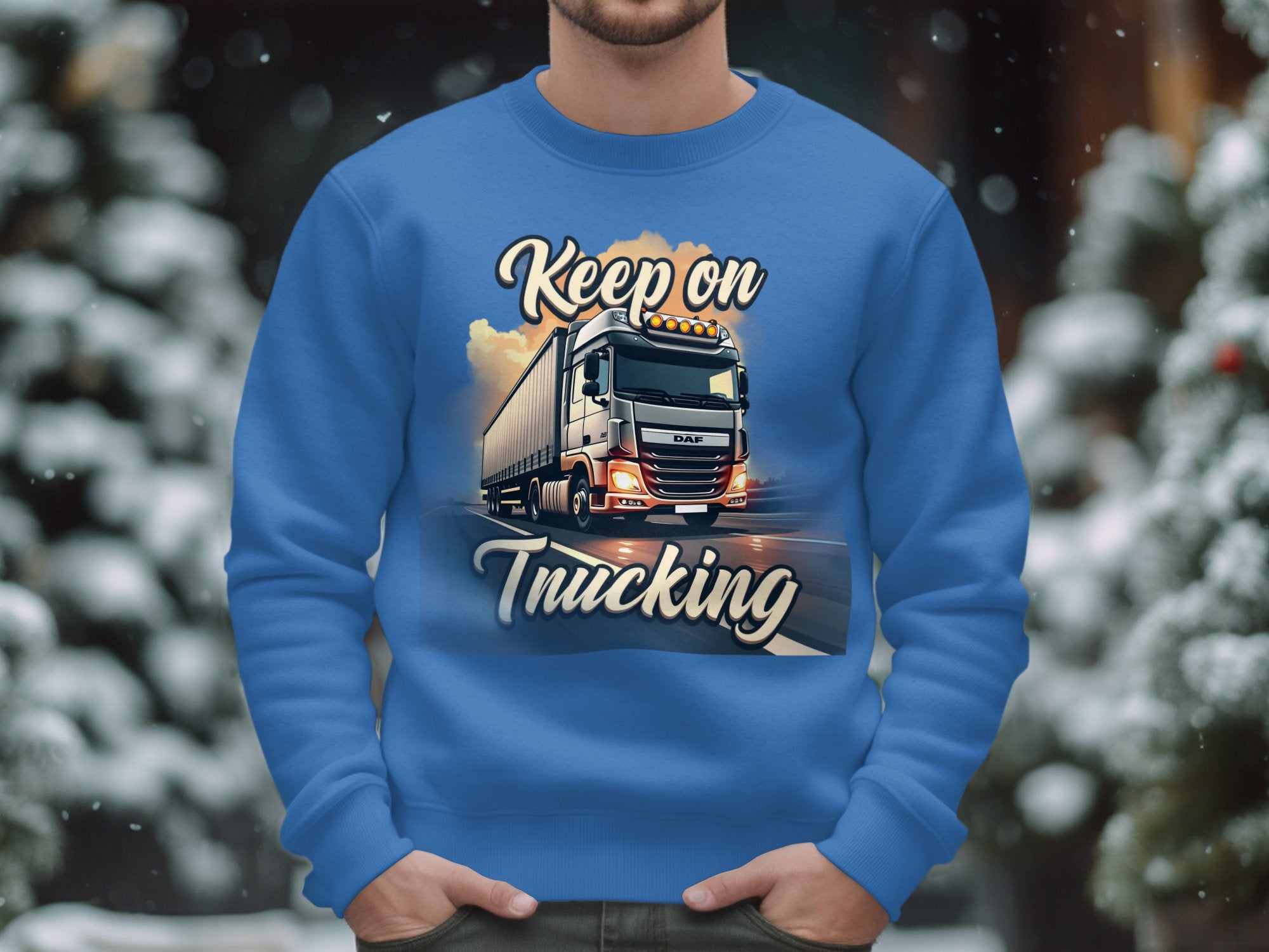 Dressed in a Garment Graphics sweatshirt featuring Keep on Trucking and a bold truck design, an individual stands against snow-covered trees, embodying the spirit of the open road in winter.