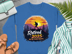 Garment Graphics presents a blue retirement sweatshirt featuring a hiker silhouette at sunset with trees. The Retired 2025, Not My Problem Anymore phrase adds charm, ideal for unisex sizing. Pair it with a purse, fern, striped shirt, shoes, and watch for a complete look.