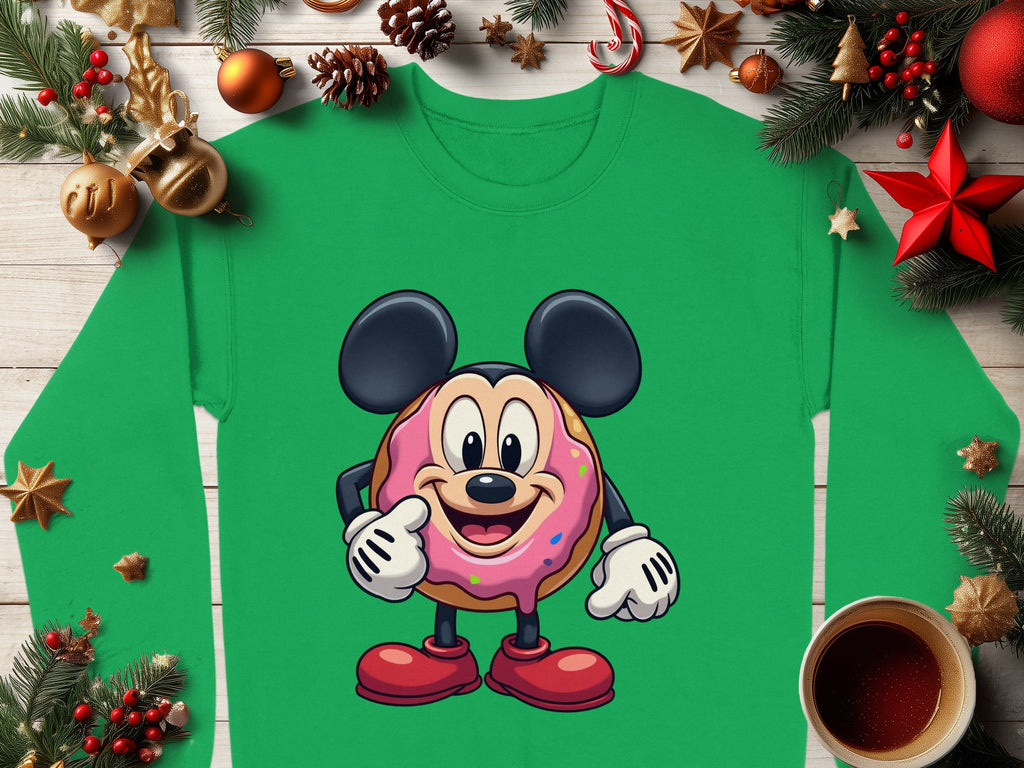 Garment Graphics quirky green sweatshirt features a large-eared cartoon character posing confidently. It is playfully designed with festive pine branches, red stars, baubles, and a cozy coffee cup on a wooden surface.