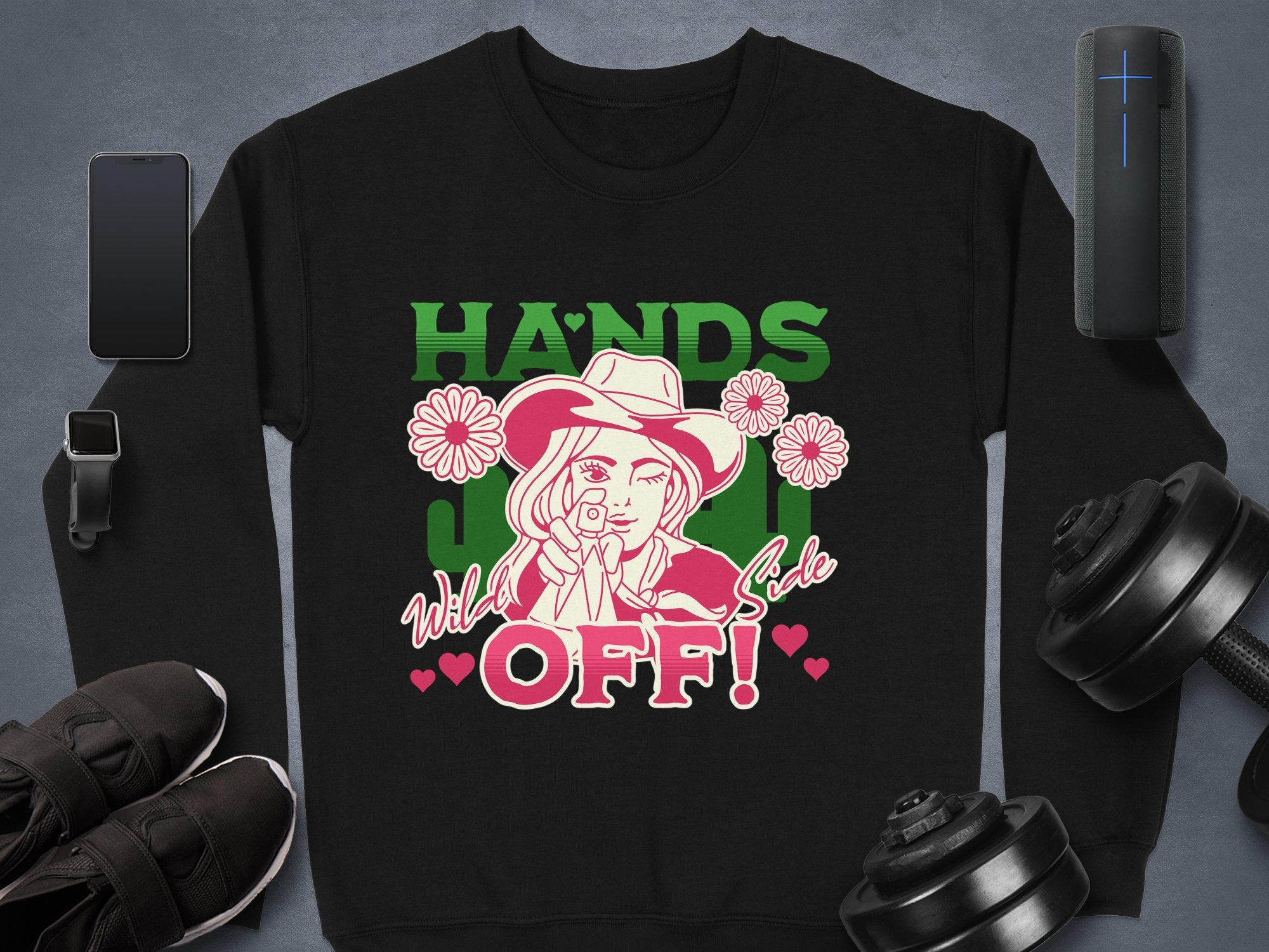 The Garment Graphics Wild Side Sweatshirt in unisex sizing features vibrant artwork of a person wearing a hat adorned with flowers, surrounded by the phrases HANDS OFF! and Wild Side, alongside objects like a smartphone, smartwatch, speakers, sneakers, and dumbbells.