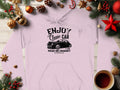 A Garment Graphics hoodie rests on a wooden surface adorned with festive pine branches, baubles, cinnamon sticks, and tea. This classic fit features a vintage car graphic with the text Enjoy Classic Car, Vintage Ride Community, celebrating community spirit.