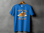 A blue Garment Graphics t-shirt, ideal for family sizing, hangs on a wooden hanger against a gray backdrop. It features an illustrated spicy pie slice with eyes and mouth, surrounded by the phrase Hot & Spicy You Wanna a Piece of Me?.
