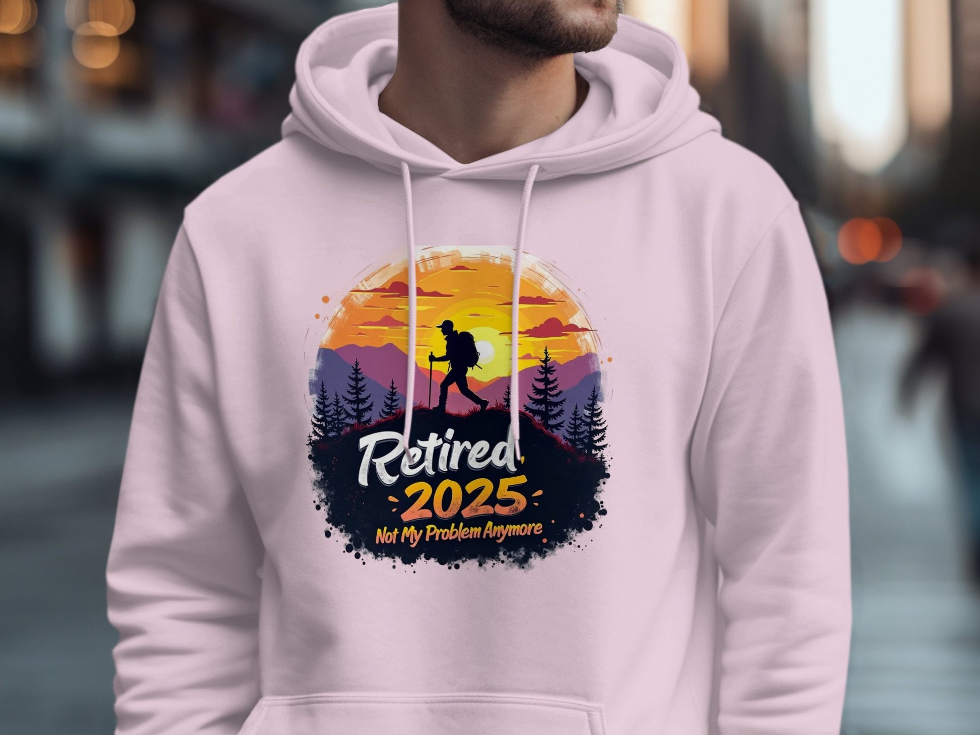 A person is wearing a Garment Graphics white hoodie with a sunset mountain design. It shows a hiker silhouette against majestic peaks and trees, with the text Retired 2025, Not My Problem Anymore—ideal for hiking enthusiasts and serene escape lovers.