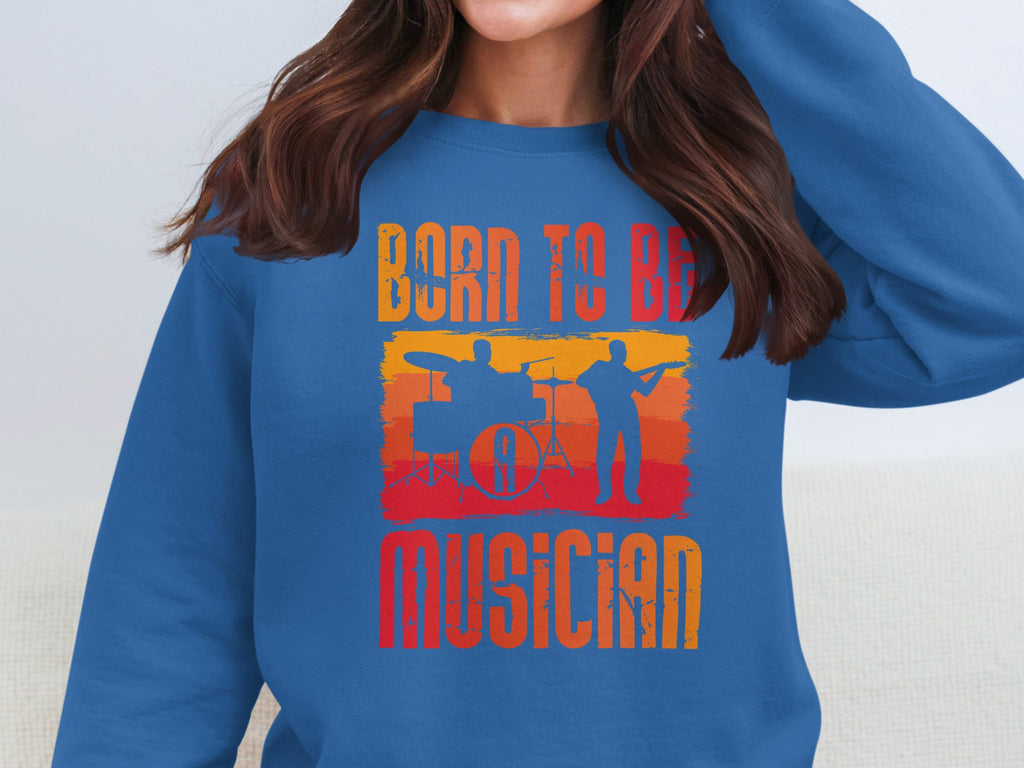 A music enthusiast sports Garment Graphics blue unisex sweatshirt with Born to Be Musician and silhouettes of a drummer and guitarist against a sunset gradient, capturing the passion and harmony of the musical spirit.