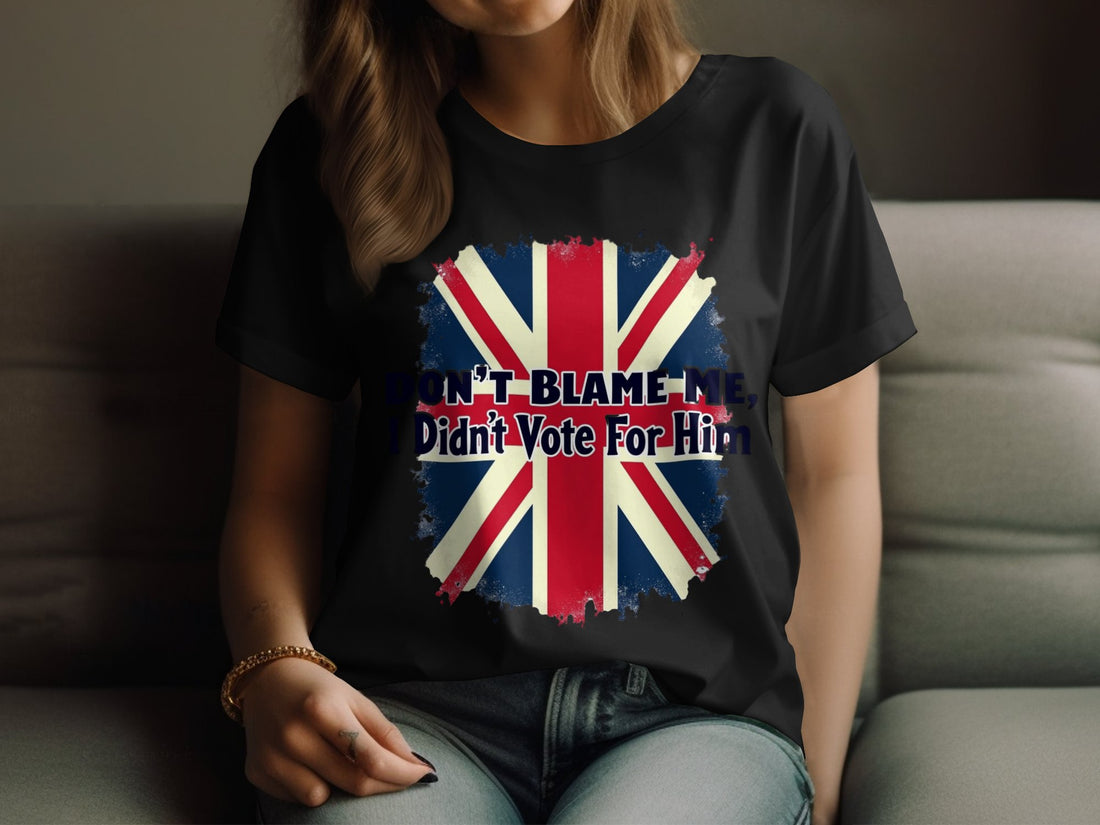 The Garment Graphics white t-shirt, made from 100% cotton, features the Union Jack and Dont Blame Me, I Didnt Vote For Him. Amid wrapped gifts, red and white decorations, a knitted sweater, and a candy cane on a wooden surface,this shirt stands out boldly.