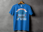A Garment Graphics blue fishing T-shirt hangs on a wooden hanger against a gray background. Ideal for anglers, it features multicolored text: Id rather have a bad day fishing than a good day at work, making it an excellent gift for any fishing enthusiast.