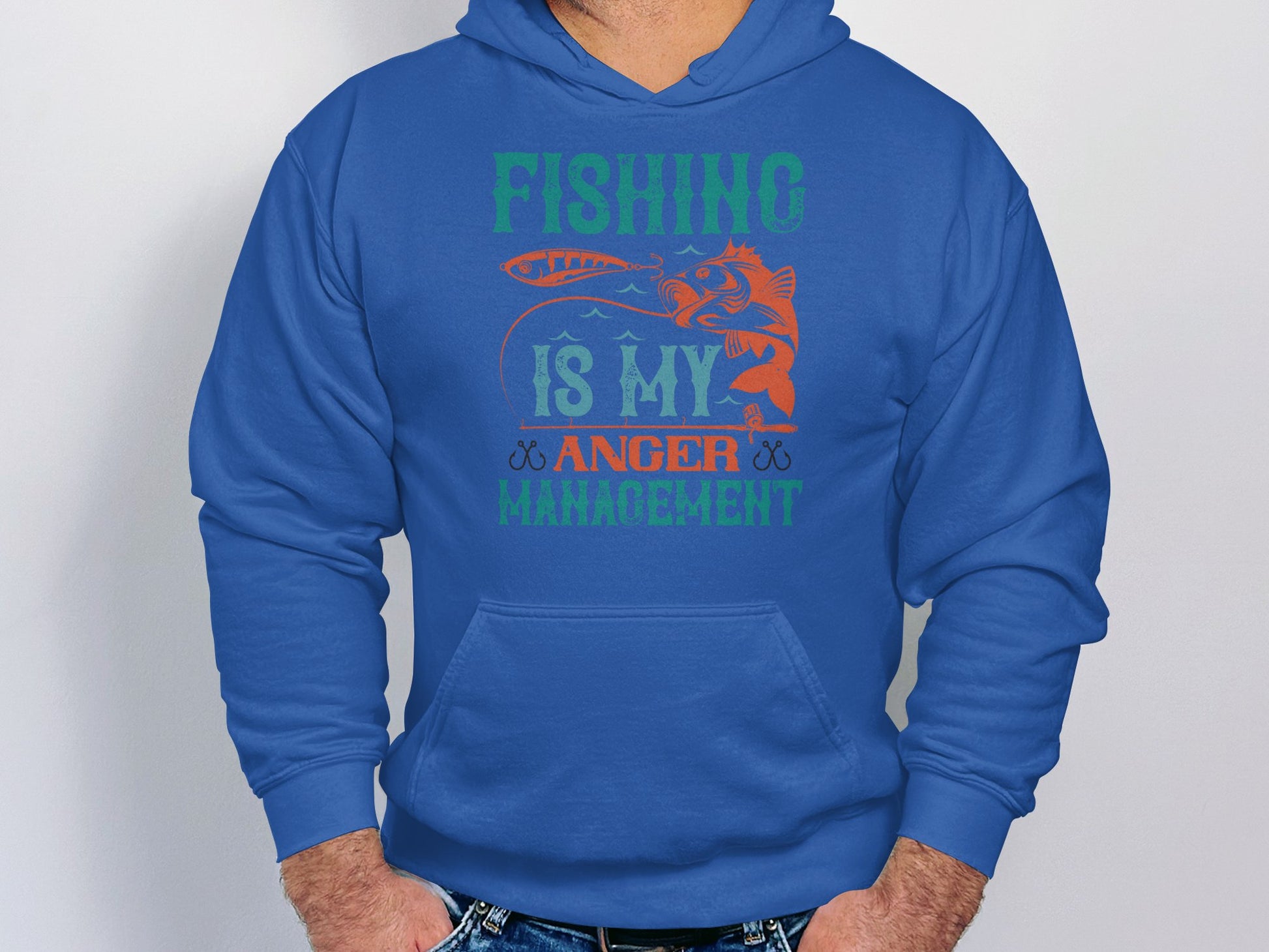 In front of a simple light backdrop, a person wears a blue hoodie from Garment Graphics Anglers Wardrobe collection. Fishing is my anger management is written in vibrant green, orange, and blue letters with a fish illustration—a perfect choice for any fishing enthusiast.