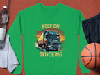 A Garment Graphics green graphic sweatshirt with Keep On Trucking truck design is on a surface beside a basketball, black shorts, a white towel, and a water bottle.