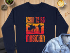 A navy unisex sweatshirt by Garment Graphics, featuring Born to be a Musician and a drummer silhouette, lies on wood with a denim shirt, latte cup, succulent, and rock nearby for music lovers.