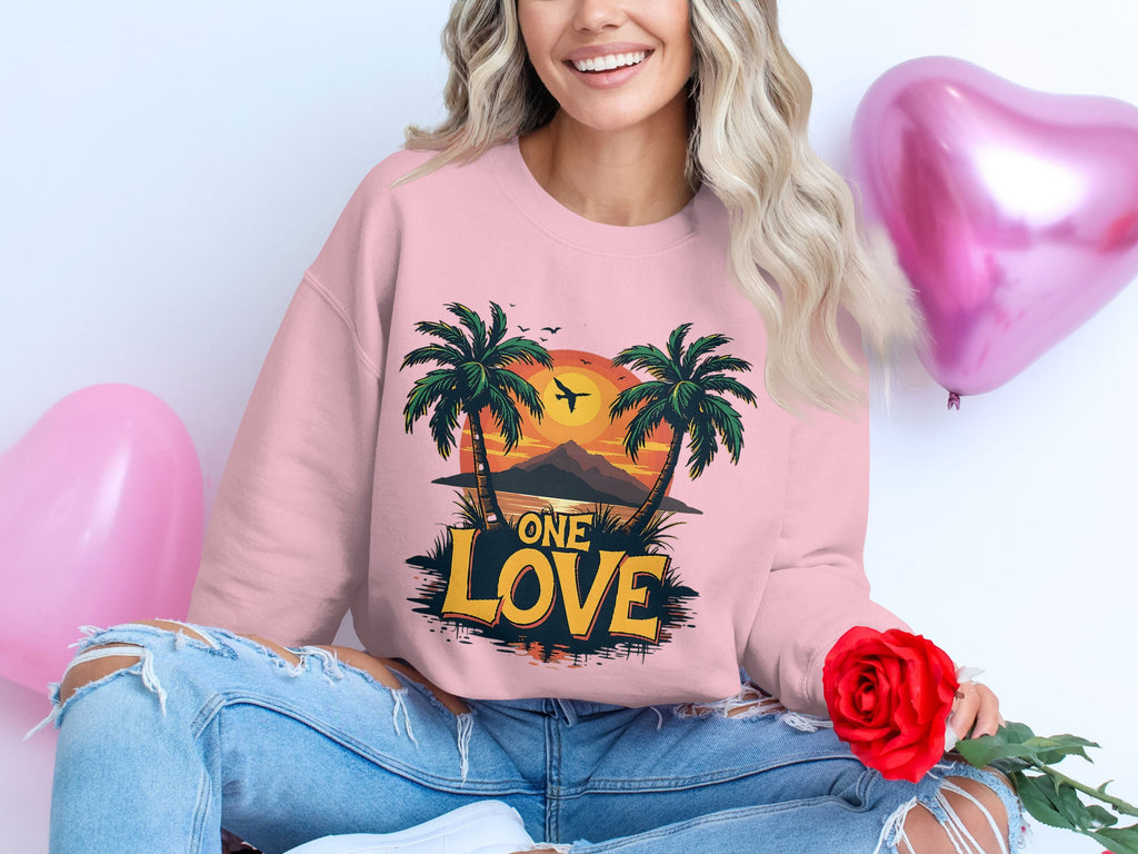 A person with wavy hair wears a Garment Graphics pink sweatshirt featuring palm trees and One Love Sunset design, holding a red rose while sitting beside heart-shaped balloons in pink and purple, perfectly complementing their ripped jeans.