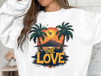 A person wears a white sweatshirt featuring a vivid design of palm trees, mountains, and the colors of the One Love Sunset from Garment Graphics.
