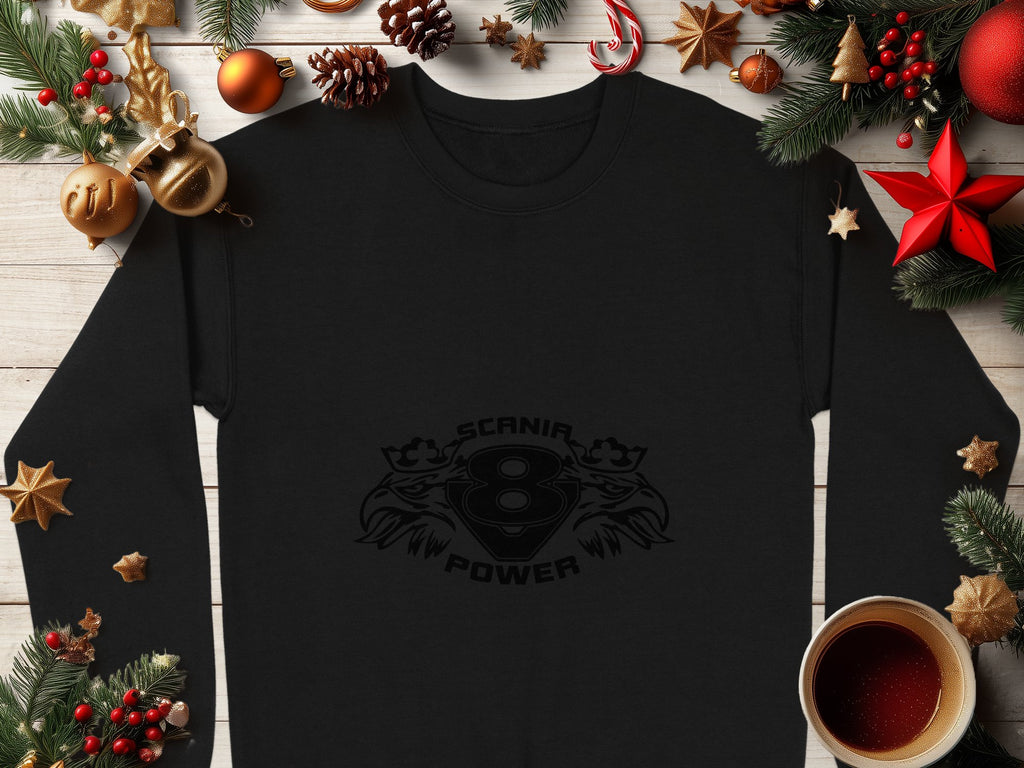 A stylish black long-sleeve shirt by Garment Graphics showcasing the Scania V8 Power design is artfully displayed with Christmas decorations such as pine cones, ornaments, stars, and a cozy coffee cup on a wooden surface, highlighting its cool print.