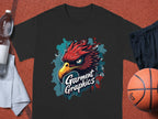 A black T-shirt with a bold red and yellow eagle design and Garment Graphics in white is showcased on an orange sports surface, accompanied by a water bottle, gray towel, black shorts, and a basketball, emphasizing its classic fit.