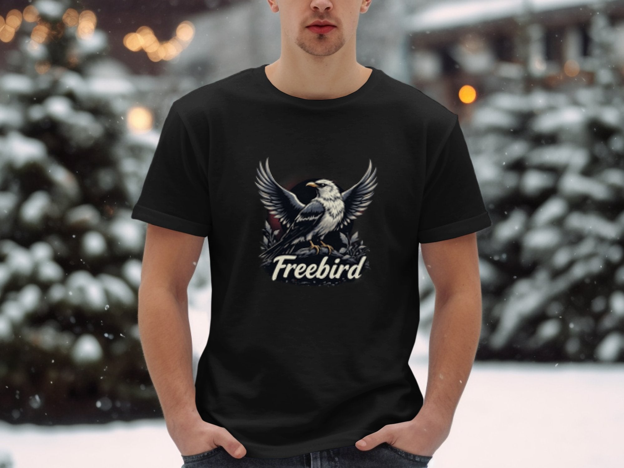 Standing outdoors in a snowy landscape, a person wears a Garment Graphics 100% cotton Freebird eagle T-shirt. With their hands in their pockets, snow-laden trees provide a perfect backdrop to the bold graphic on their shirt.