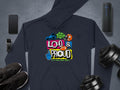 Garment Graphics navy blue hoodie features vibrant Loud & Proud text and graphics at its center, flanked by a smartphone, smartwatch, wireless speaker, black sneakers, and adjustable dumbbells on a gray backdrop—ideal for bold self-expression enthusiasts.