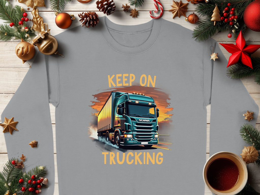 The Garment Graphics gray sweatshirt boasts a striking truck design with KEEP ON TRUCKING against a sunset. Enhanced by Christmas decorations, red stars, pine cones, and a warm coffee cup on wood, this graphic sweatshirt truly stands out.