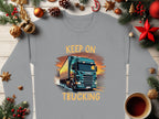 The Garment Graphics gray sweatshirt boasts a striking truck design with KEEP ON TRUCKING against a sunset. Enhanced by Christmas decorations, red stars, pine cones, and a warm coffee cup on wood, this graphic sweatshirt truly stands out.