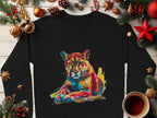 A Garment Graphics black shirt with a vibrant abstract mountain lion design is laid on wood, surrounded by Christmas decor like pine branches, cones, stars, ornaments, and coffee—ideal for unique style seekers in unisex sizing.