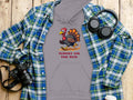 The Garment Graphics gray hoodie displays a cartoon turkey and Turkey on the Run text. Its styled with a blue plaid shirt, black headphones, a camera, and a takeaway coffee cup on rustic wood.