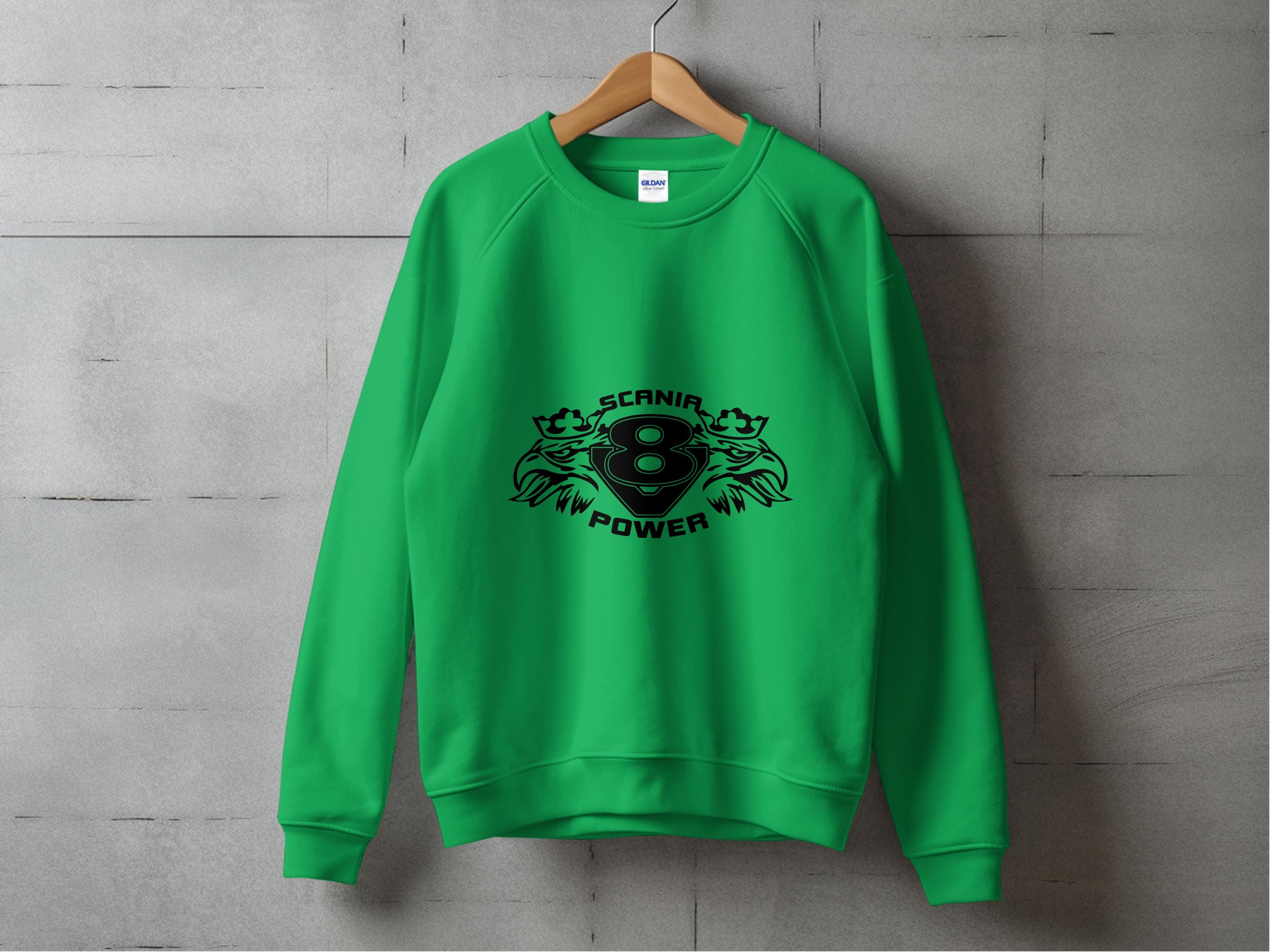 Against a gray concrete wall, a vibrant green sweatshirt by Garment Graphics is displayed, featuring the striking black Scania Power 8 logo. Two stylized frog-like creatures surround the emblem, giving it a unique and dynamic look.