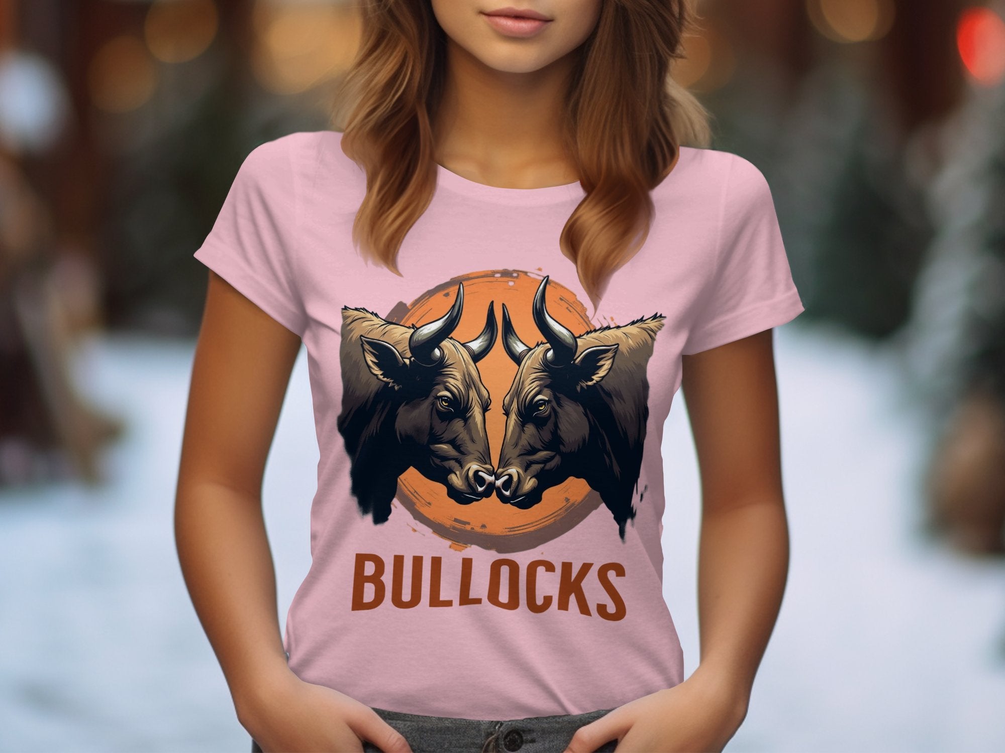 Amid a snowy scene, someone wears a Garment Graphics pink T-shirt featuring bold graphics of two bulls locking horns over an orange circle. The word BULLOCKS is below, making it ideal for lovers of striking bull illustrations.