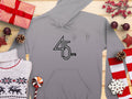 Garment Graphics hoodie, featuring a 45 RPM print for vinyl enthusiasts, is displayed with red/white gifts, pinecones, berries, candy cane, stars, and a reindeer-patterned sweater on wood. Ideal for retro music fans.