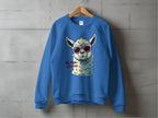 A blue unisex sweatshirt from Garment Graphics hangs on a wooden hanger against a concrete wall, featuring a whimsical illustration of a llama with red sunglasses and the playful phrase No Prob-Llama.