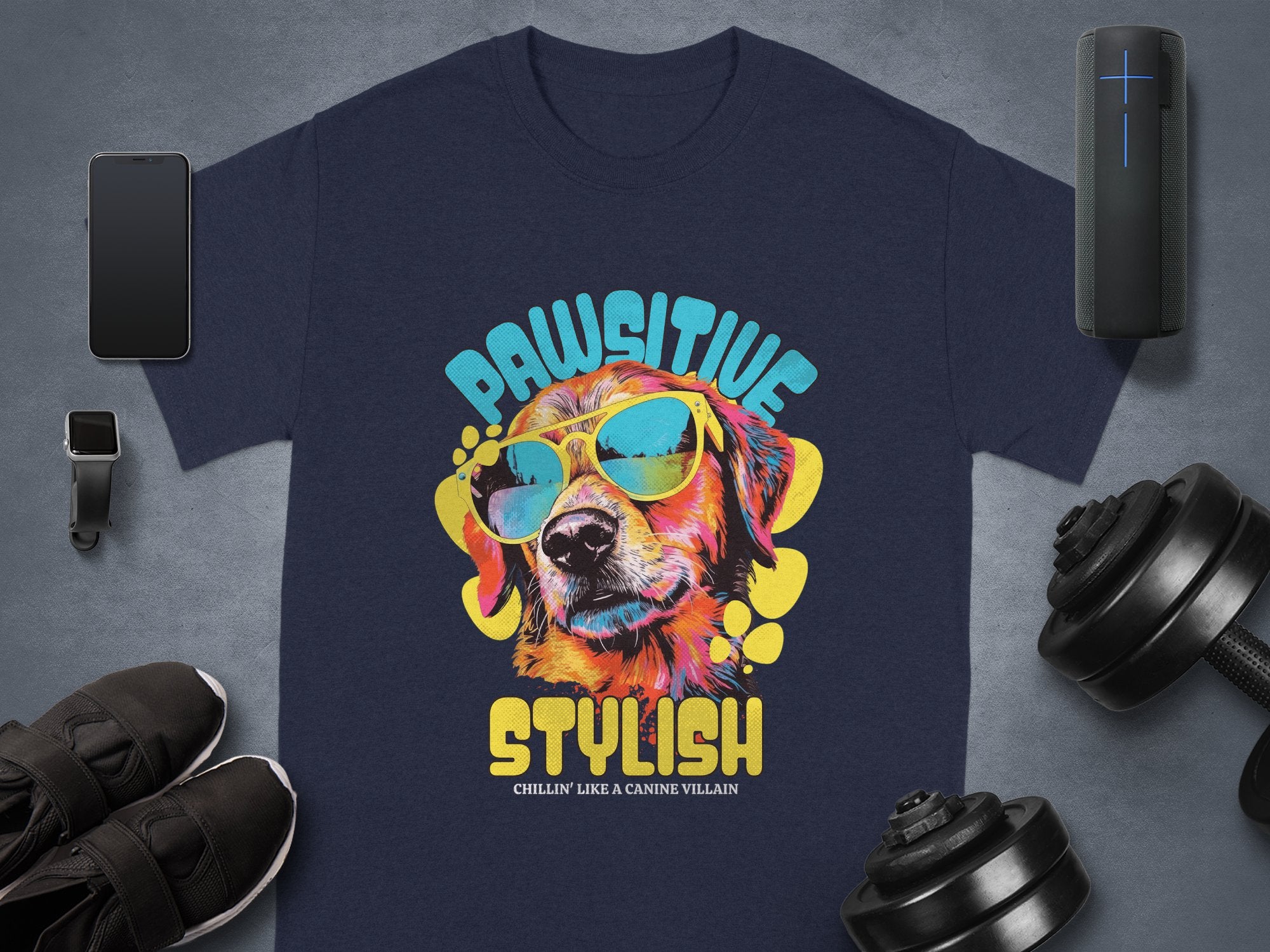 Garment Graphics offers a navy blue Dog T-shirt featuring a dog in sunglasses and the text Paw-sitive Stylish and Chillin Like A Canine Villain, paired with items like a smartphone, smartwatch, water bottle, speaker, sneakers, and dumbbells.