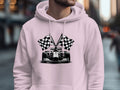 A person in a Garment Graphics white hoodie with a race car and two checkered flags stands on an urban street, surrounded by blurred buildings and bustling people, enhancing the racing theme.