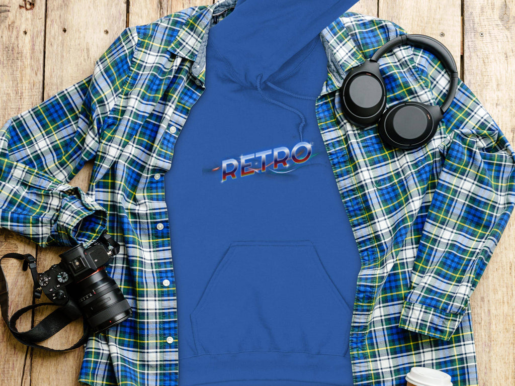 A vivid blue hoodie with Retro in stylized letters from Garment Graphics is laid flat on a wooden surface, surrounded by a plaid shirt, headphones, a camera, and a lidded coffee cup for a trendy modern vibe.
