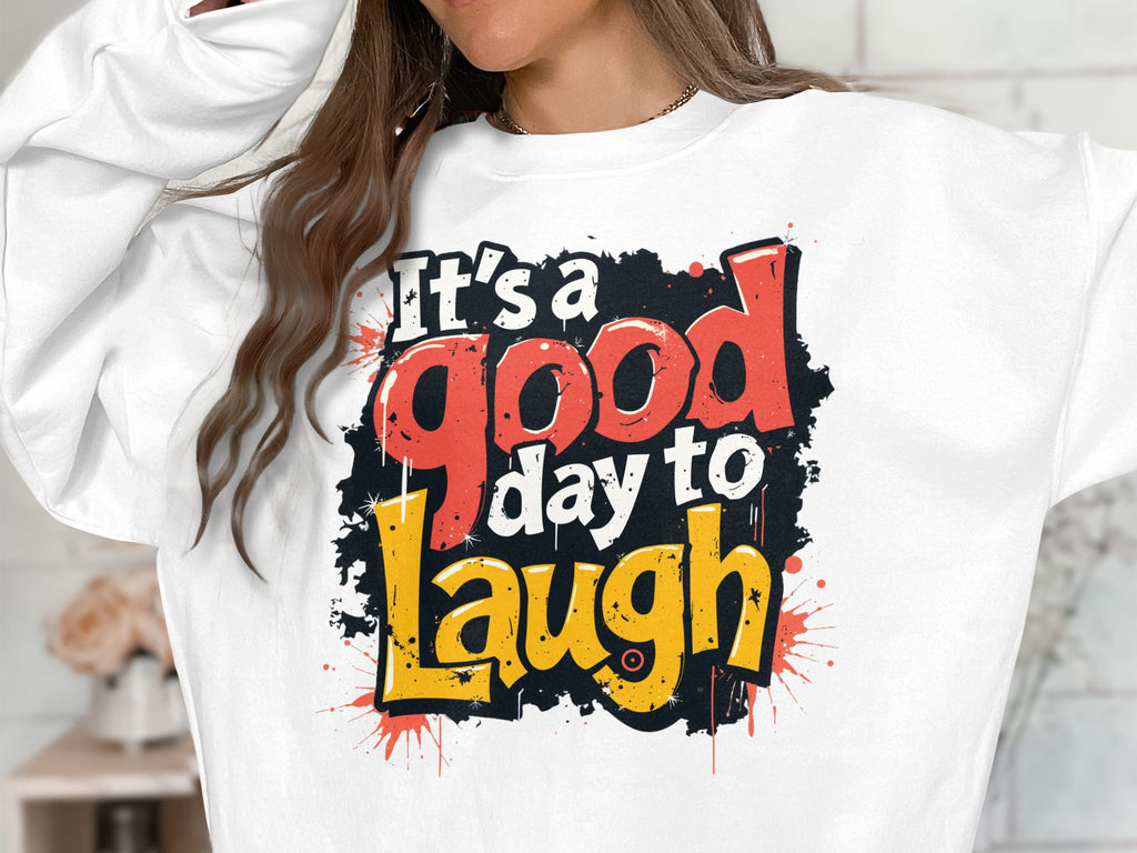 A person is wearing a Garment Graphics sweatshirt with a colorful Its a good day to laugh text in red, yellow, and black. The bold design stands out on this unisex piece made from medium-heavy fabric, while their face remains hidden.