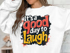 A person is wearing a Garment Graphics sweatshirt with a colorful Its a good day to laugh text in red, yellow, and black. The bold design stands out on this unisex piece made from medium-heavy fabric, while their face remains hidden.