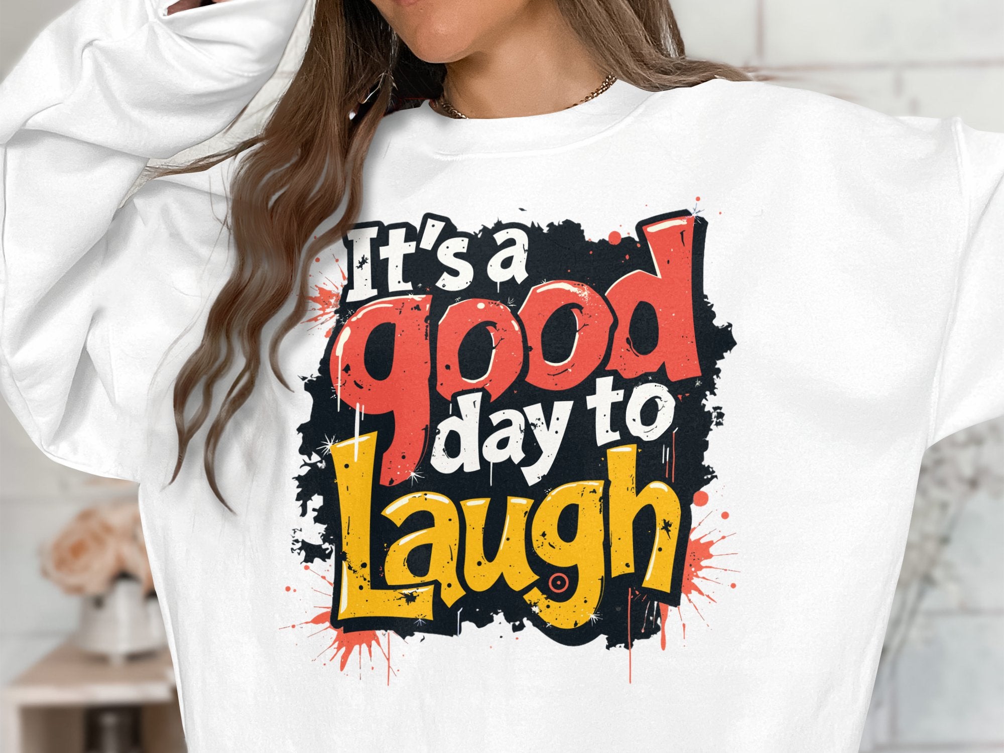 A person is wearing a Garment Graphics sweatshirt with a colorful Its a good day to laugh text in red, yellow, and black. The bold design stands out on this unisex piece made from medium-heavy fabric, while their face remains hidden.